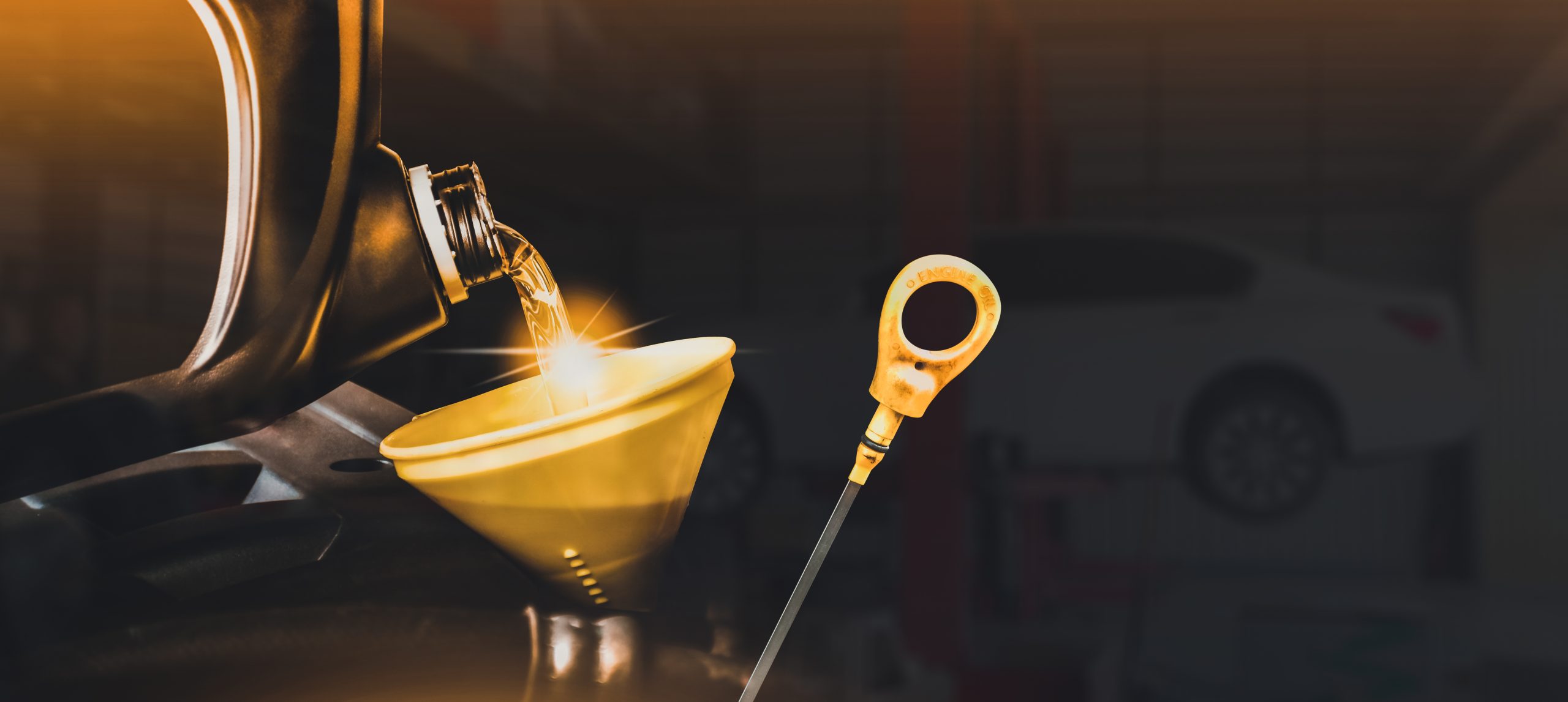 The image depicts motor oil being poured into a funnel with an oil dipstick next to it, likely during an oil change.