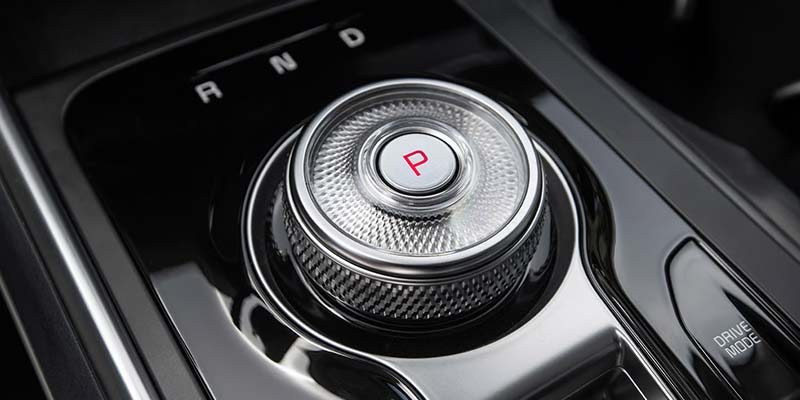 A car's rotary gear selector with a chrome finish and a red P for park in the center, on a black console.