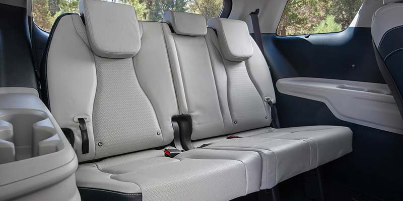 View of a light gray car interior with three back seats, headrests, seatbelts, and a cup holder console.