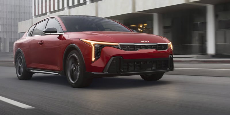 Red Kia K4 sedan driving on city street