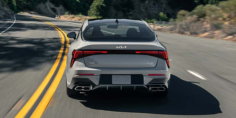 Rear view of a silver sedan driving on a winding road.
